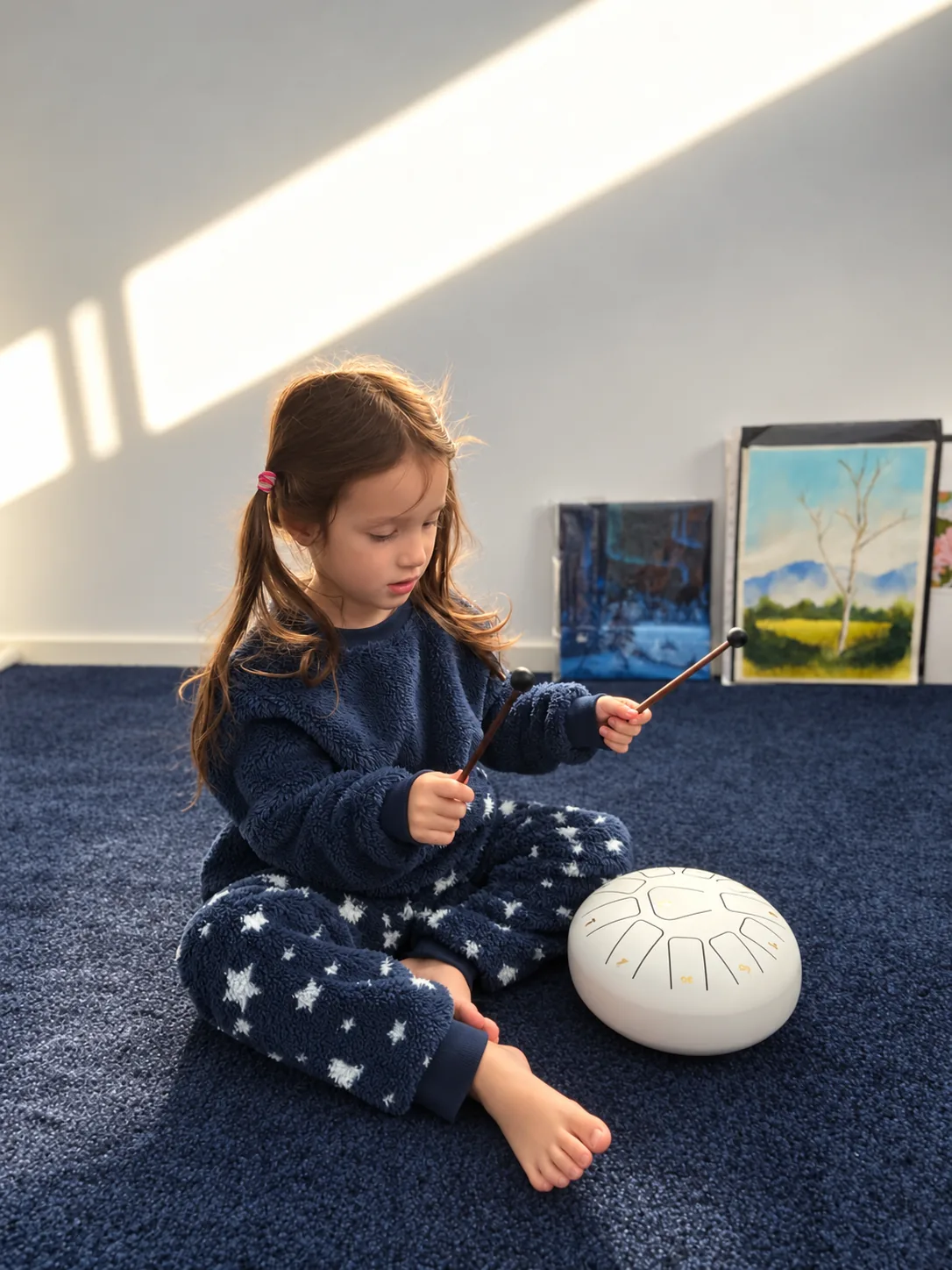 A child holding two mallets beside a white tongue drum
