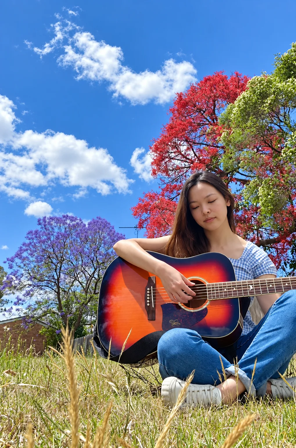 A woman seated outdoors playing an acoustic guitar beneath colourful trees
