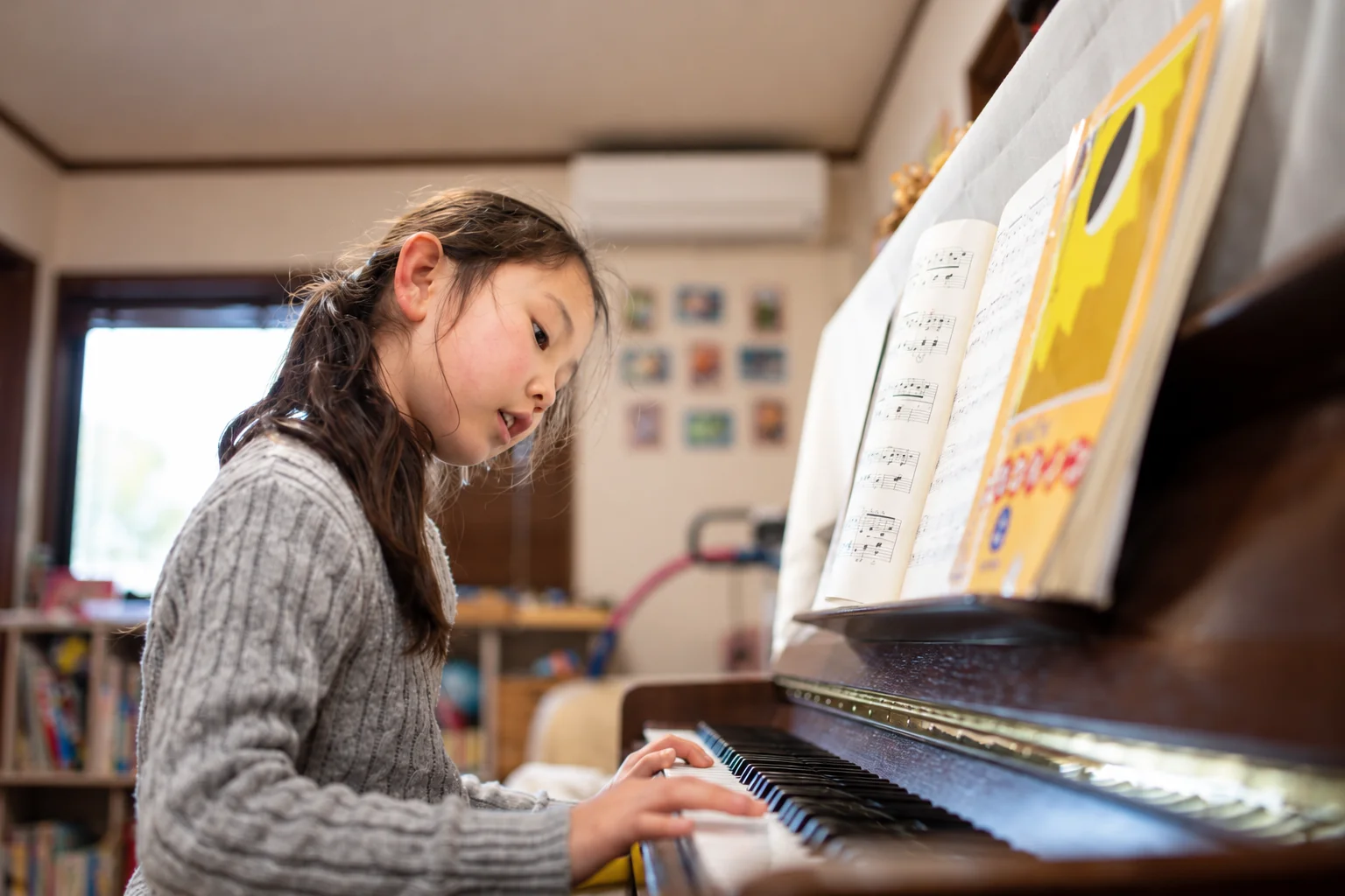 A child reading sheet music and practising at an upright piano