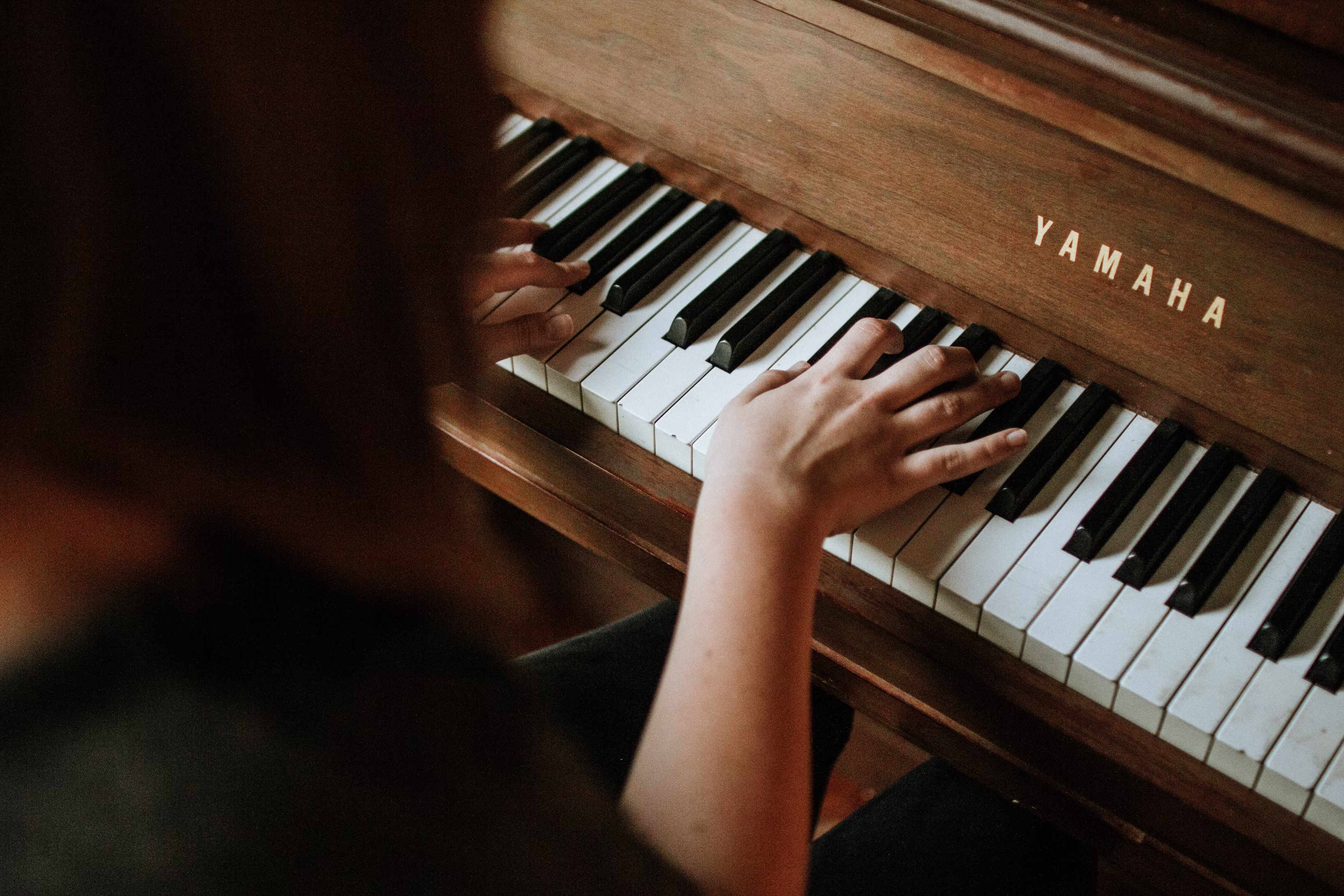 Two hands playing a wooden upright piano