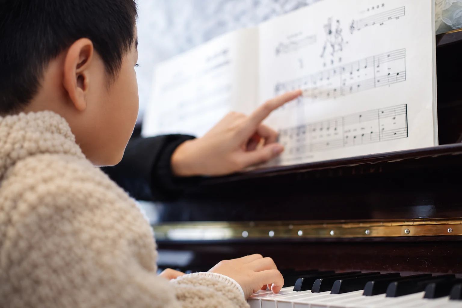 A child at a piano while a teacher points to the sheet music